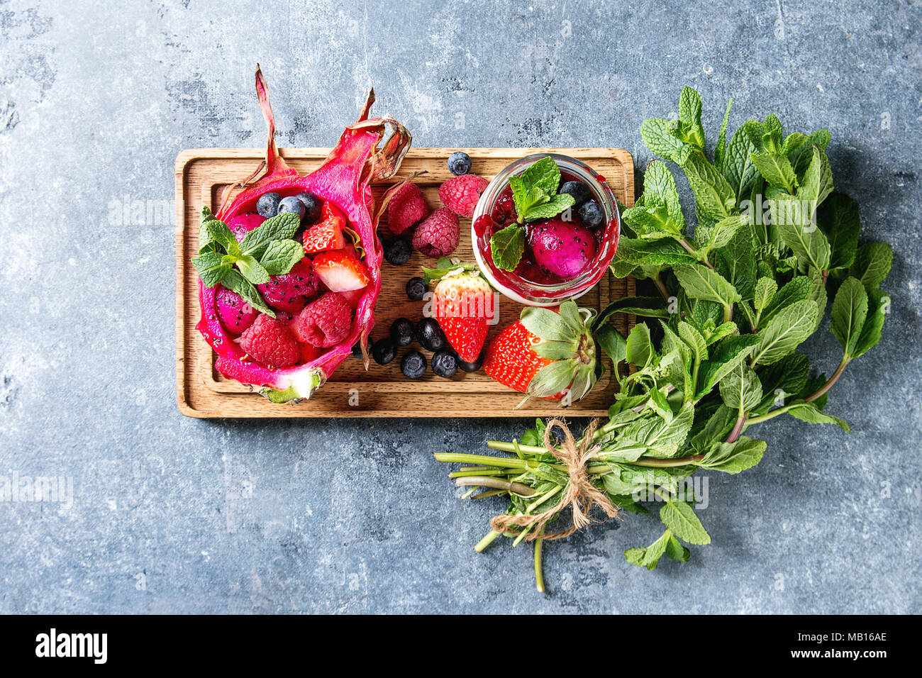 Vegan ensalada de frutas con fresas y menta en rosa dragon fruit con ingredientes por encima en madera sirviendo junta azul sobre fondo de textura. Principio V Foto de stock