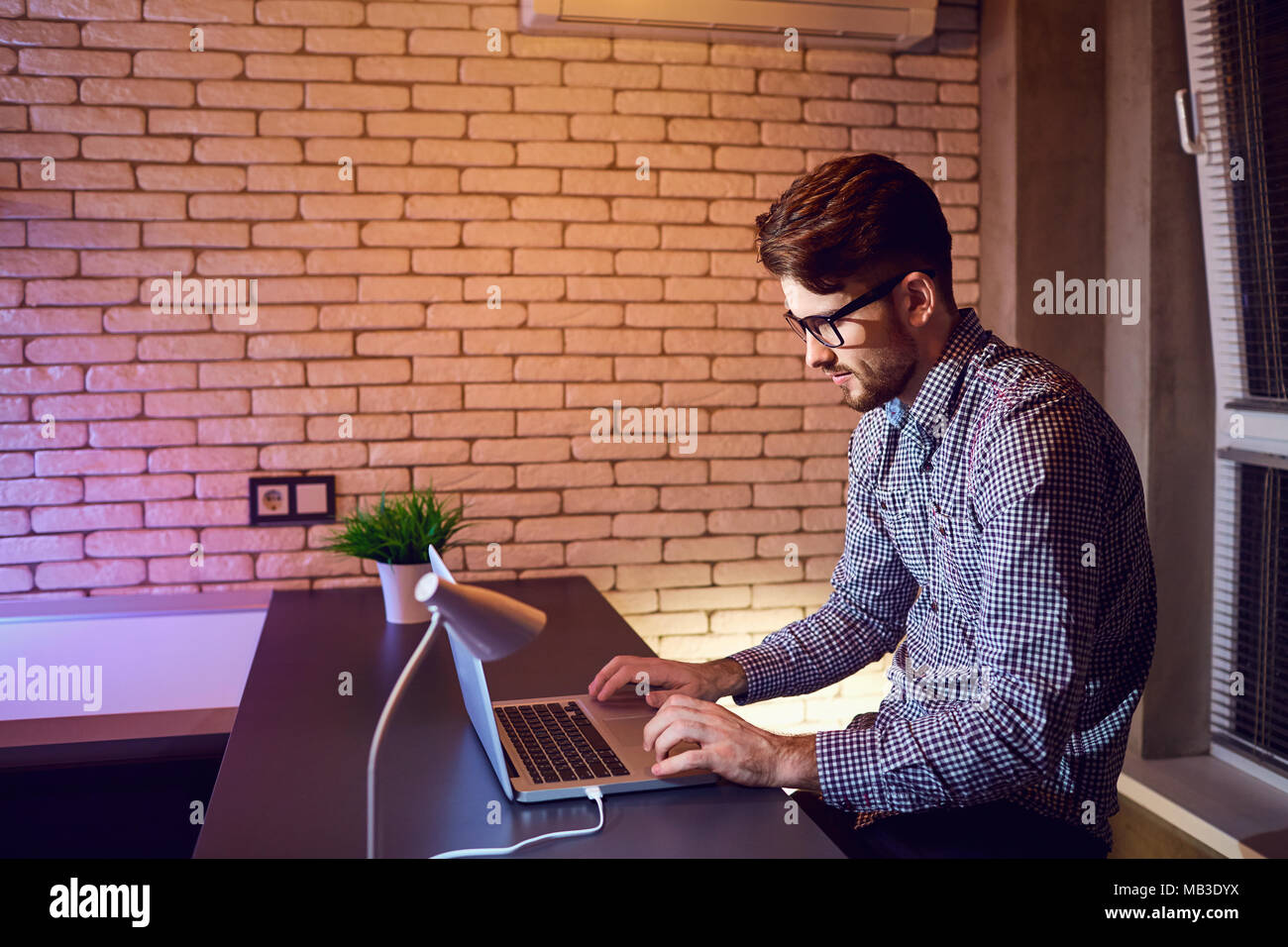 Un hombre barbado freelance con una laptop funciona en la noche. Foto de stock