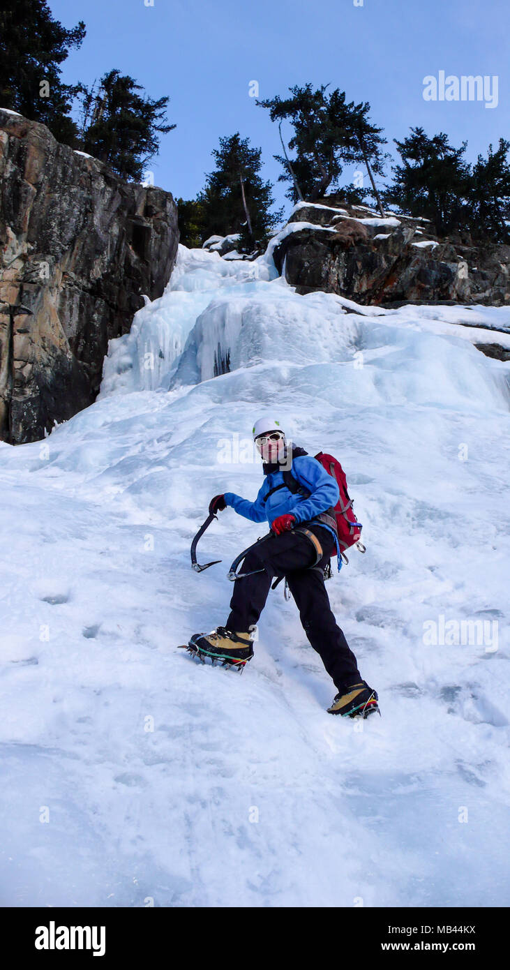 Macho escalador de hielo en una chaqueta azul en una hermosa cascada congelada la escalada en los Alpes en invierno profundo Foto de stock