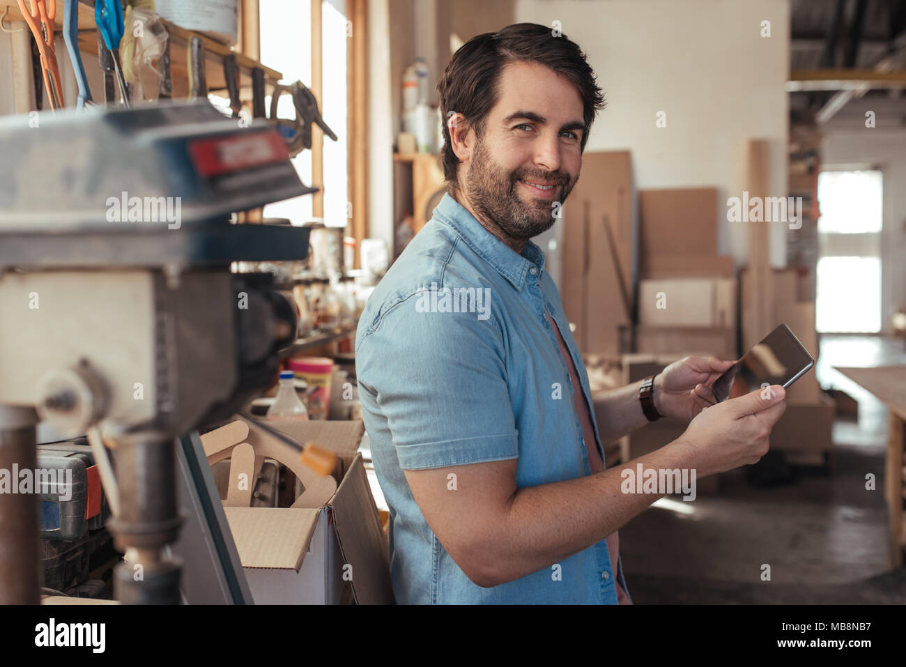 Sonriendo con un tablet artesanal en su taller de carpintería Foto de stock