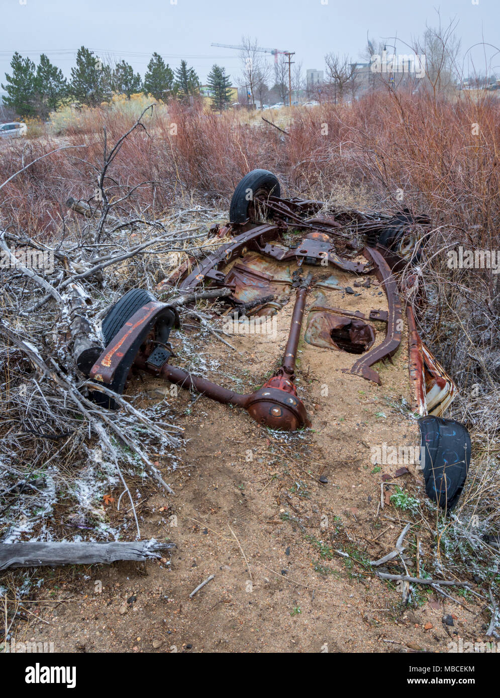 Tren de aterrizaje automático oxidados parcialmente enterrada en la arena de un arroyo cercano. Un contraste con la construcción de nuevos edificios en la distancia, Colorado. Foto de stock