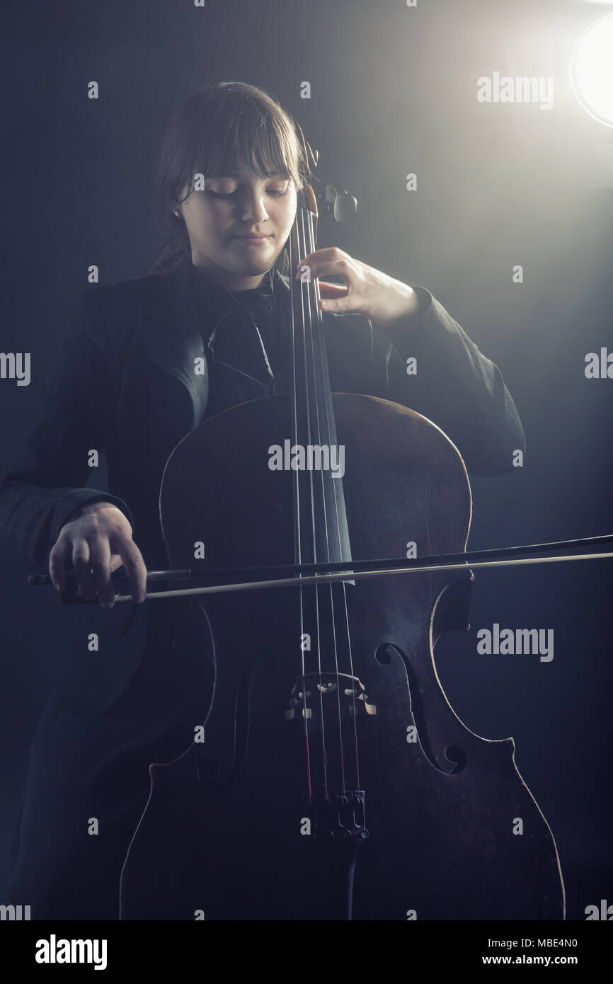 La violonchelista tocando música clásica en el cello contra un fondo negro Foto de stock