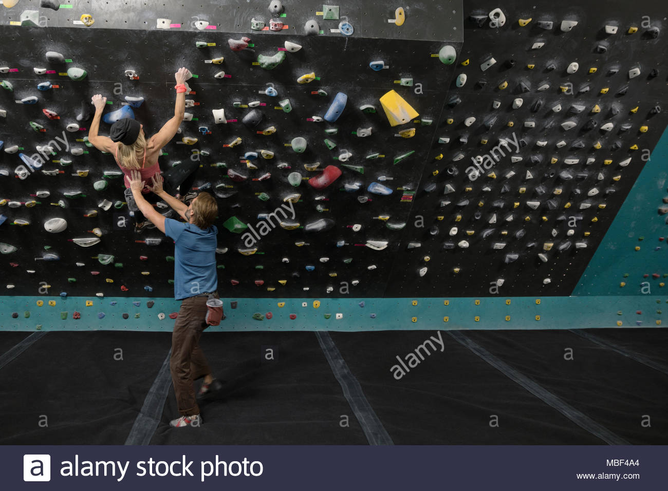Escalador macho manchado, que apoyan a las mujeres escalador muro de escalada en el gimnasio de escalada Foto de stock
