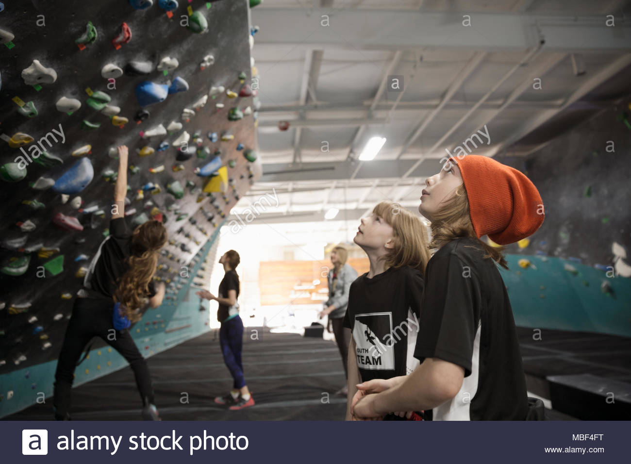 Curioso chico y chica escaladores mirando hacia arriba en la pared de escalada en el gimnasio de escalada Foto de stock