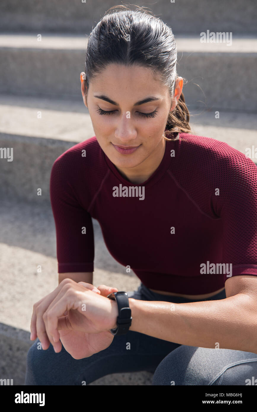 Hermosa morenita en escaleras mirando a ver o fitness tracker Foto de stock