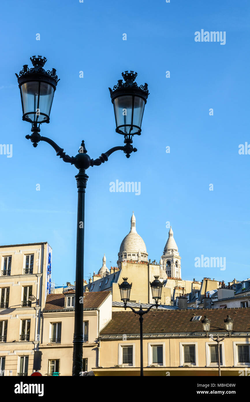 La cúpula y campanario cuadrado de la Basílica del Sagrado Corazón en París que sobresalen por encima de los tejados de los edificios de la calle con una luz en el primer plano. Foto de stock