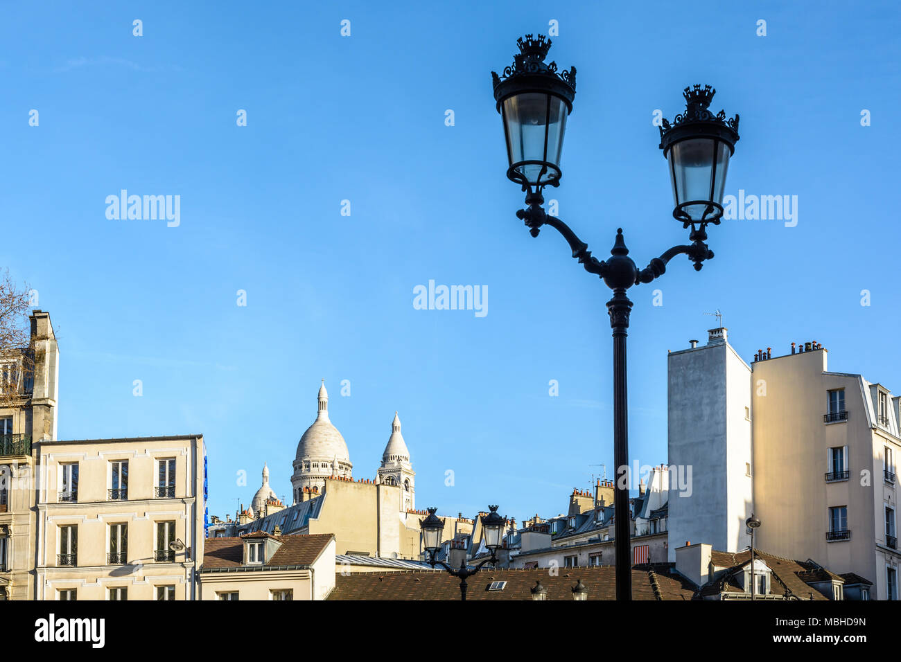 La cúpula y campanario cuadrado de la Basílica del Sagrado Corazón en París que sobresalen por encima de los tejados de los edificios de la calle con una luz en el primer plano. Foto de stock