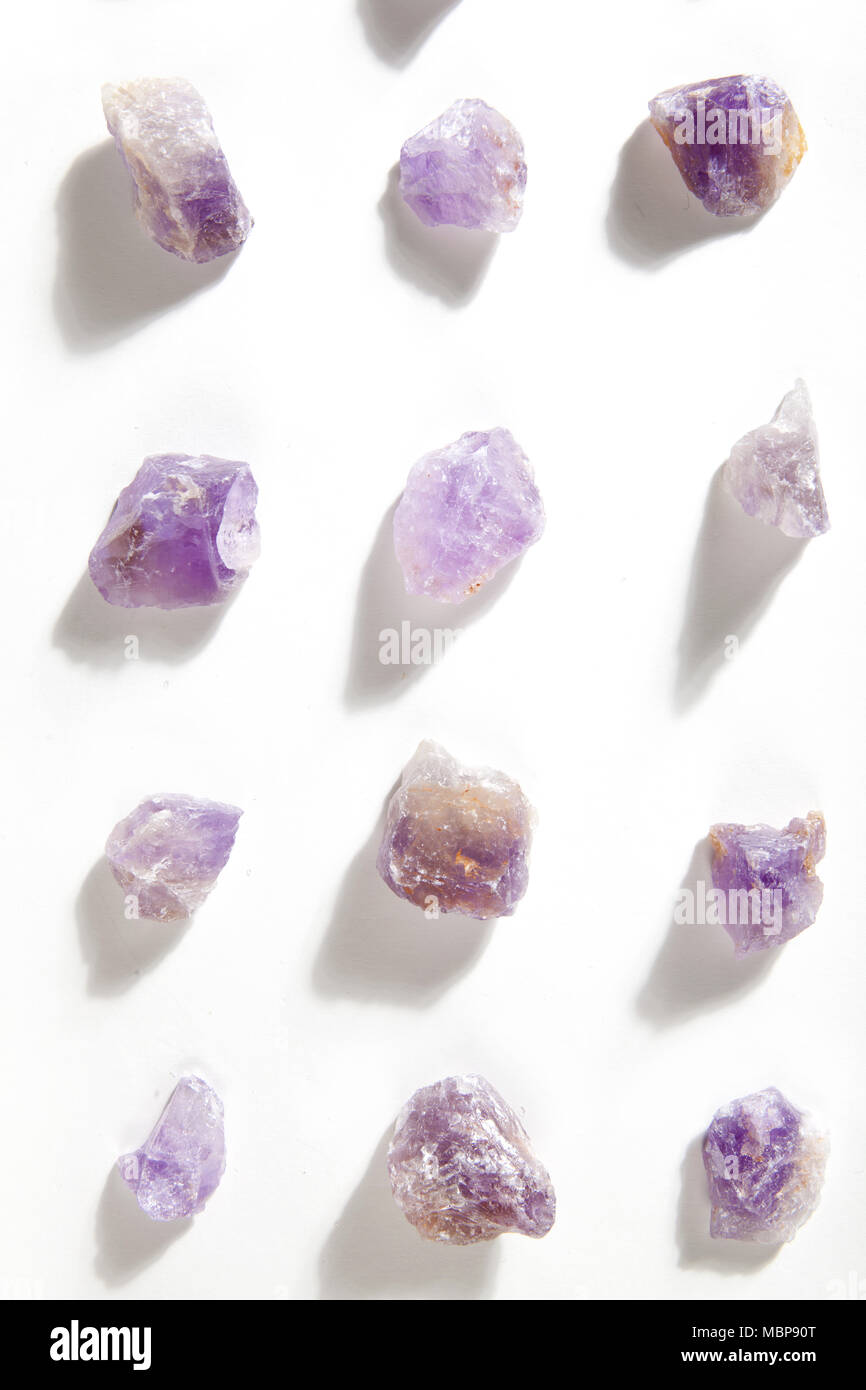Varios pedazos de materias amatista alineadas sobre un fondo blanco. Color mínimo la fotografía de modos de vida. Foto de stock
