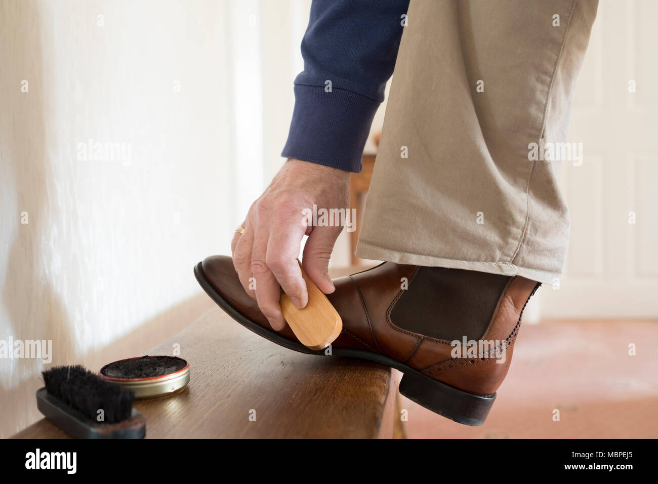 El hombre con el pie en el banquillo limpiando sus botas con boot polaco y  un cepillo Fotografía de stock - Alamy
