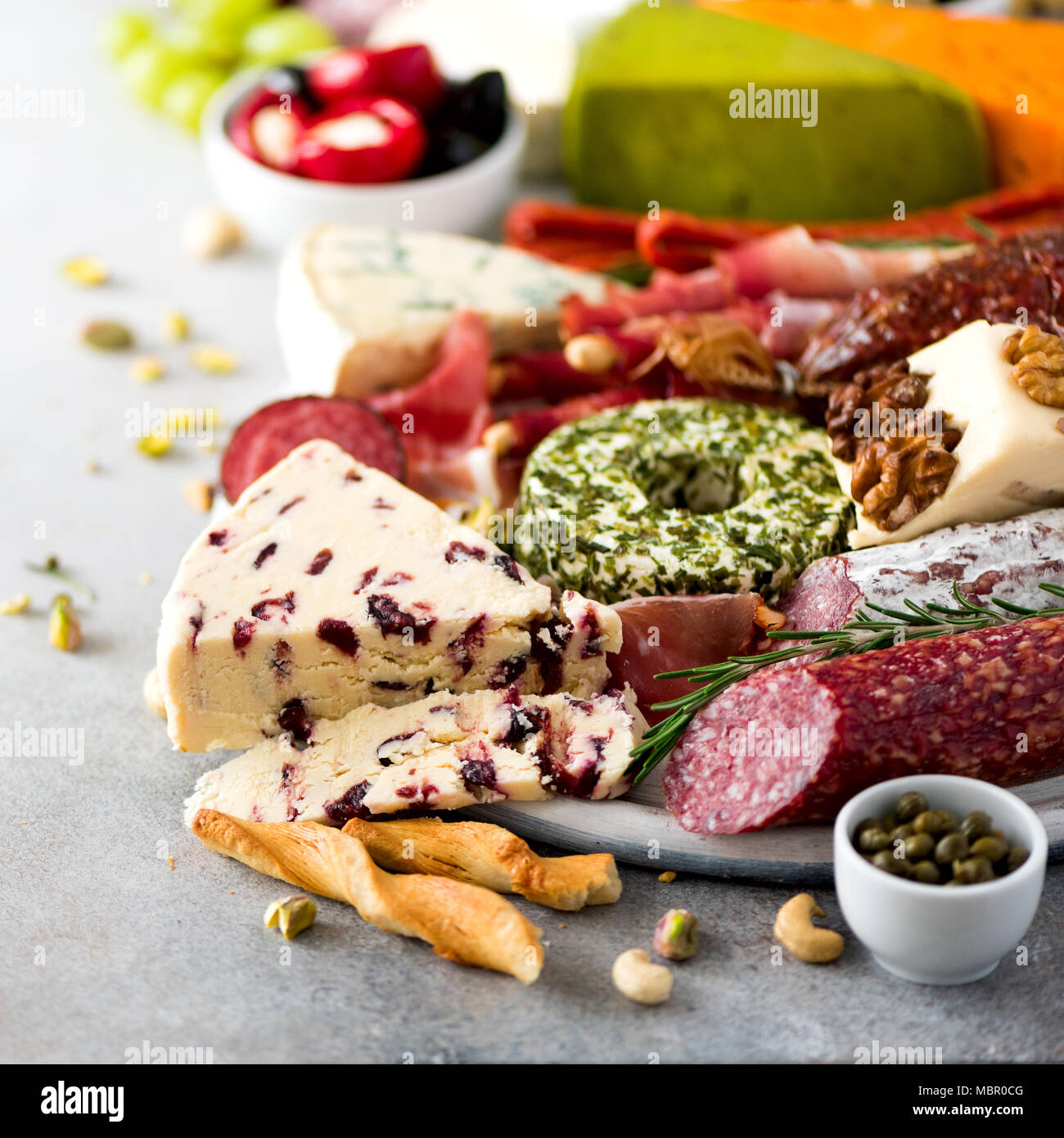 Antipasto italiano tradicional, la tabla de cortar con salami, fría la carne ahumada, Jamón, jamón, queso, aceitunas, alcaparras sobre fondo gris. Aperitivo de queso y carne. Recortar cuadrados Foto de stock