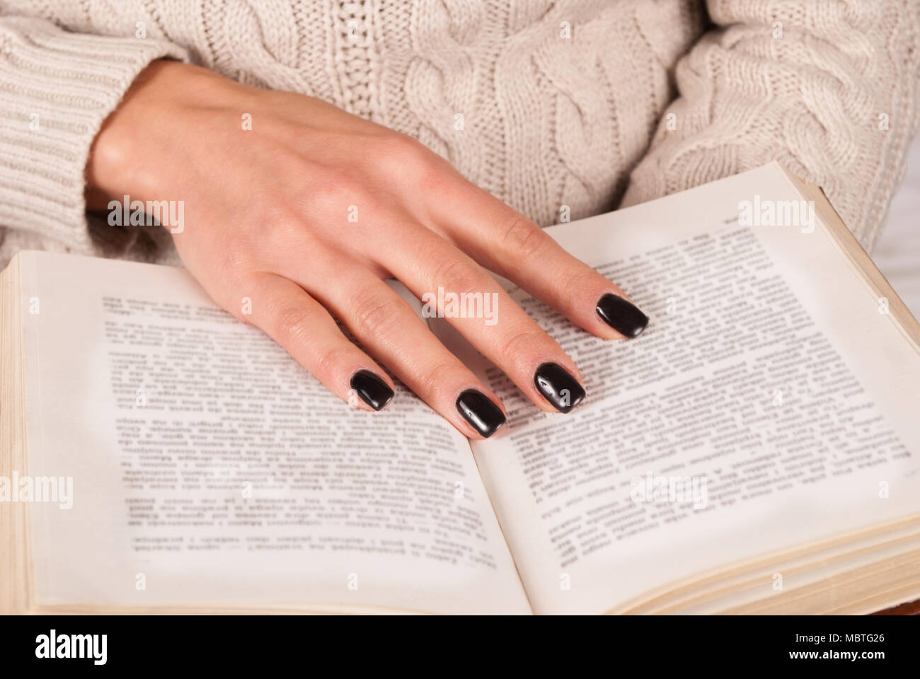 Chica mano con uñas negras en el libro, mujer de suéter libro de lectura,  cerrar Fotografía de stock - Alamy