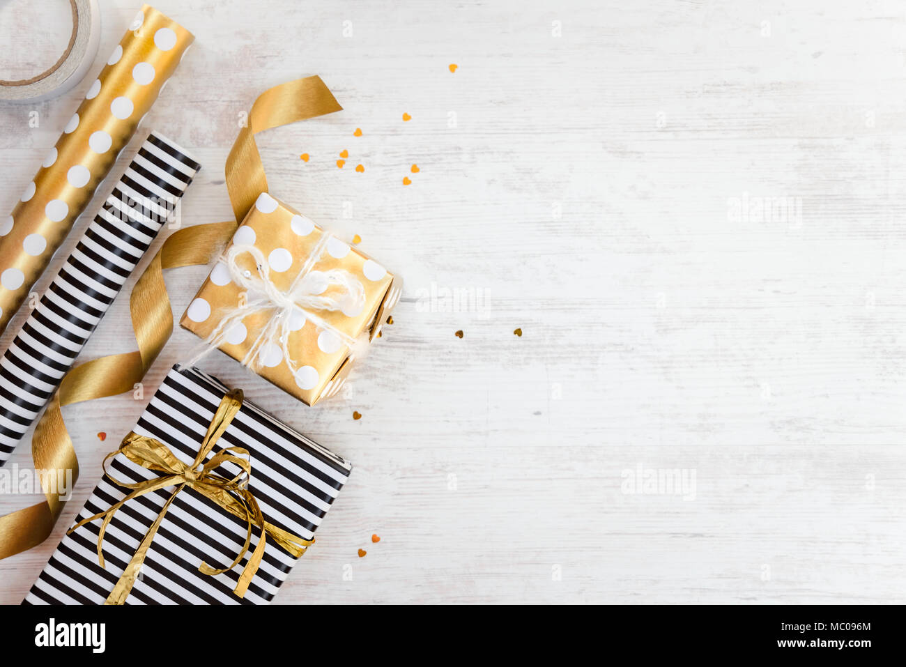 Cajas de regalos envueltos en rayas blancas y negras y doradas salpicadas de papel y materiales de embalaje de madera blanca sobre un fondo antiguo. Espacio vacío. Foto de stock