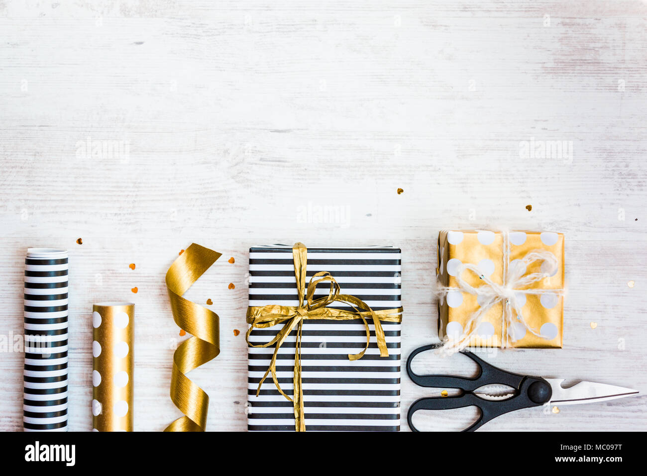 Cajas de regalos envueltos en rayas blancas y negras y doradas salpicadas de papel y materiales de embalaje de madera blanca sobre un fondo antiguo. Espacio vacío. Foto de stock