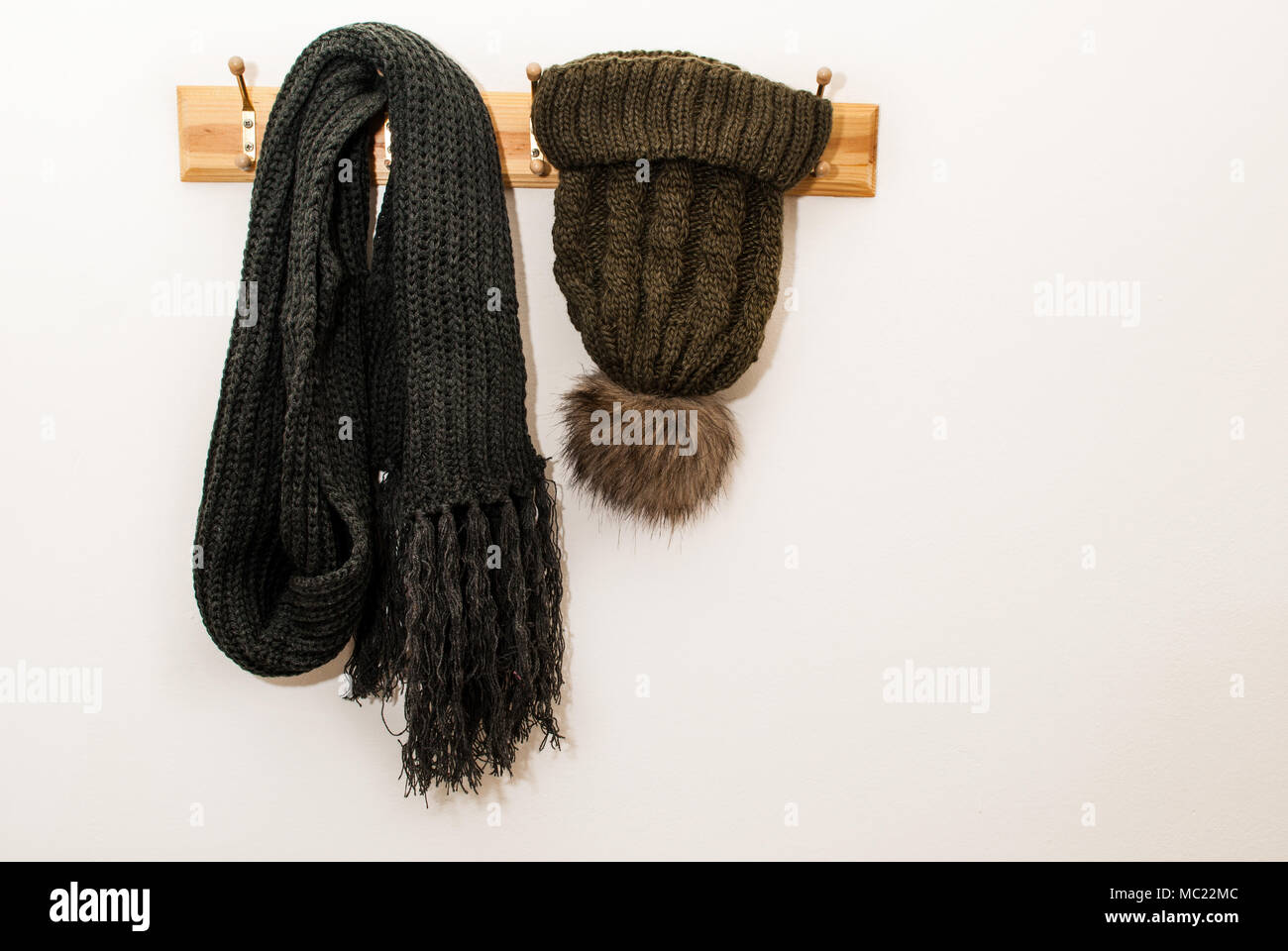 Invierno bufanda de lana y cap con una bola peluda y colgado en un perchero sobre fondo blanco. Foto de stock