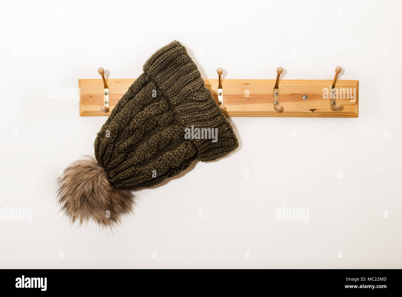 Tapón de lana de invierno con una bola peluda colgando de un perchero sobre fondo blanco. Foto de stock