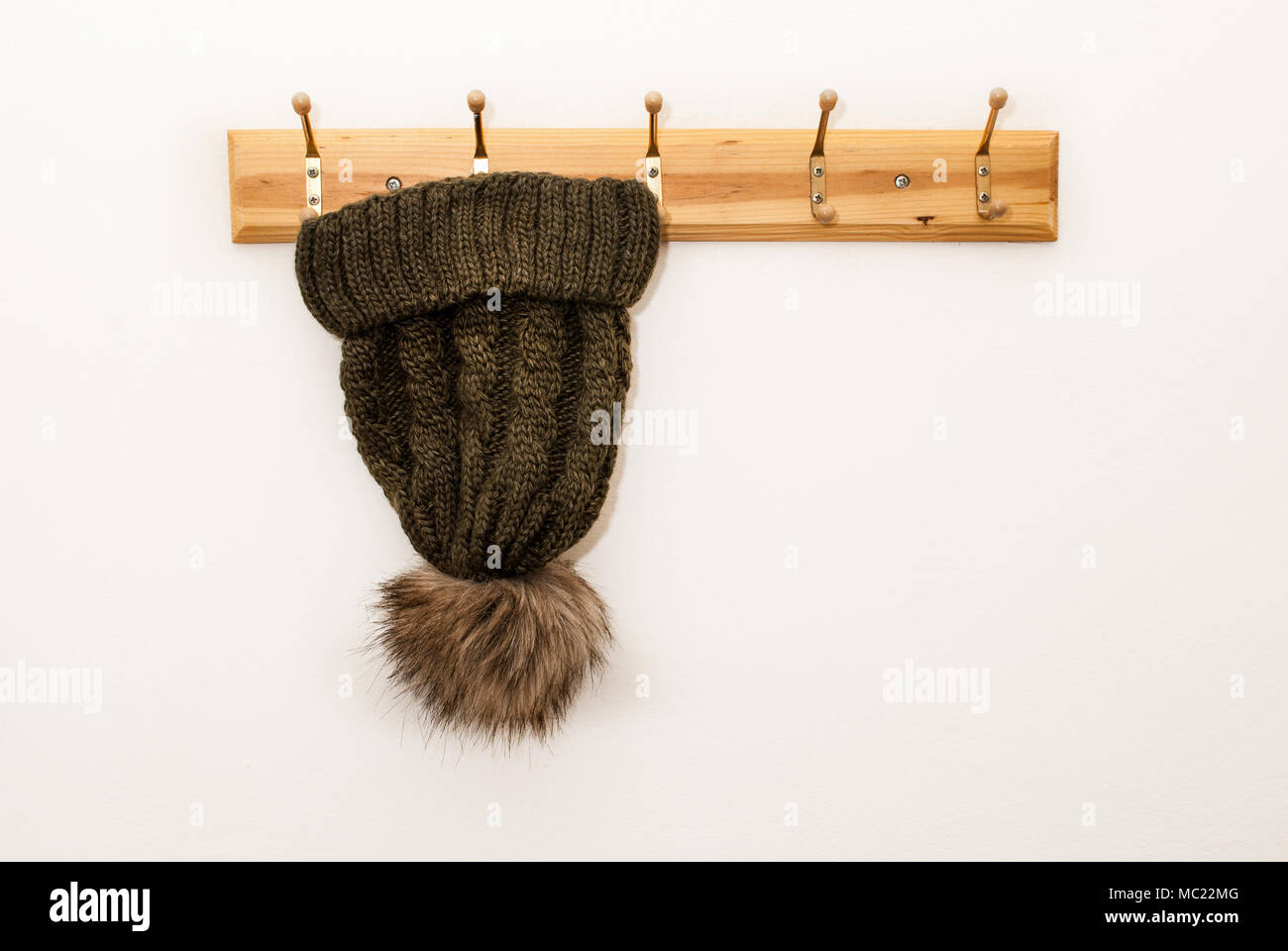 Tapón de lana de invierno con una bola peluda en color verde colgando de un perchero sobre fondo blanco y espacio para el texto Foto de stock