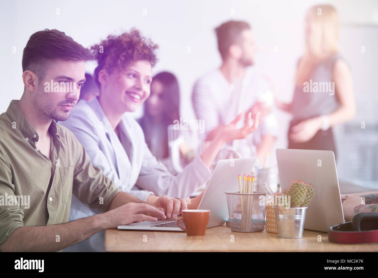 Un empresario trabajando en su computadora portátil y su mujer sonriendo y hablando junto a él Foto de stock