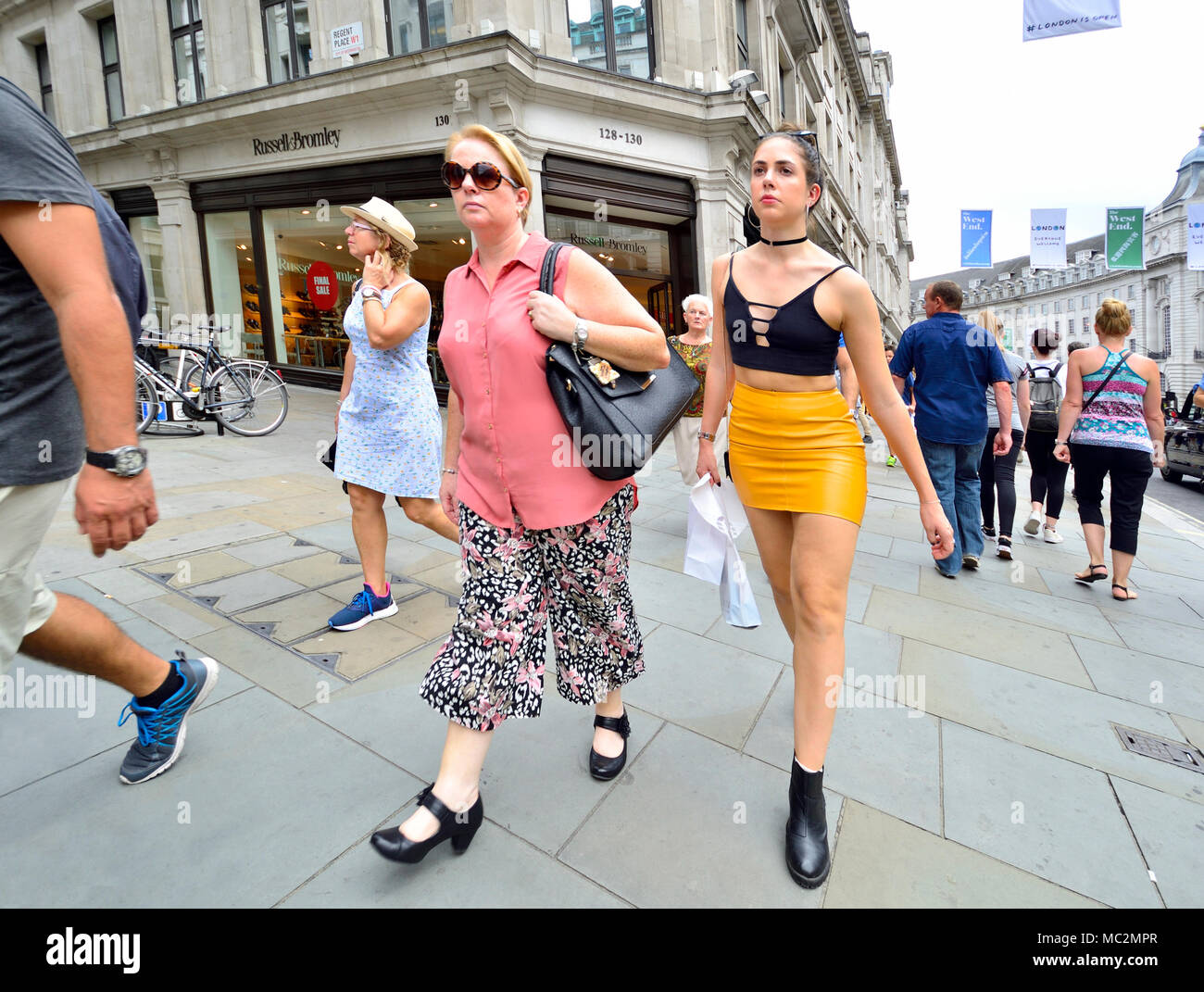 Londres, Inglaterra, Reino Unido. La mujer en Regent Street - contrastantes estilos de moda. Mujer joven en plástico / falda de cuero Foto de stock