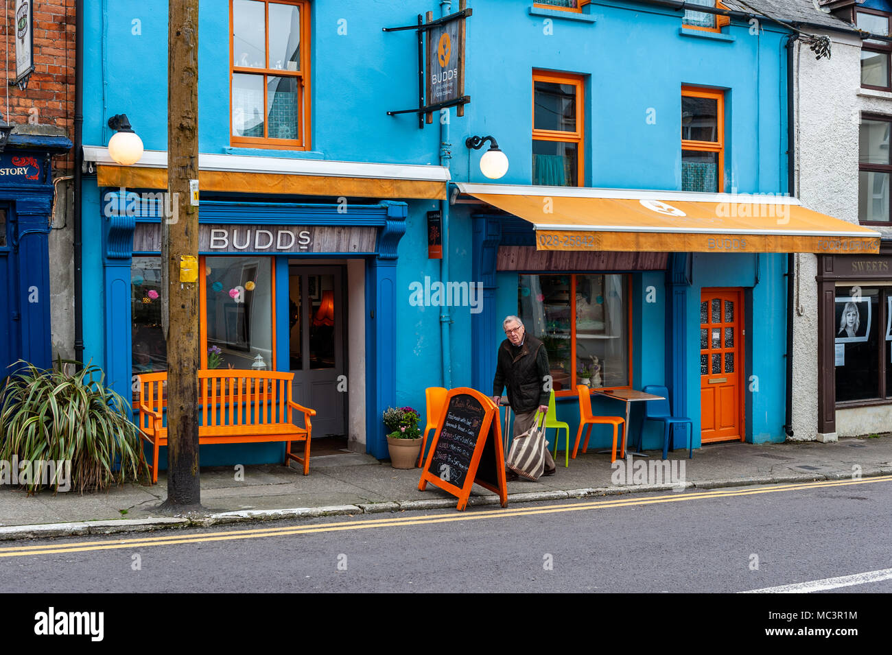 Hombre caminando pasado Restaurante Budds, Main Street, Ballydehob, Condado de Cork, Irlanda. Foto de stock