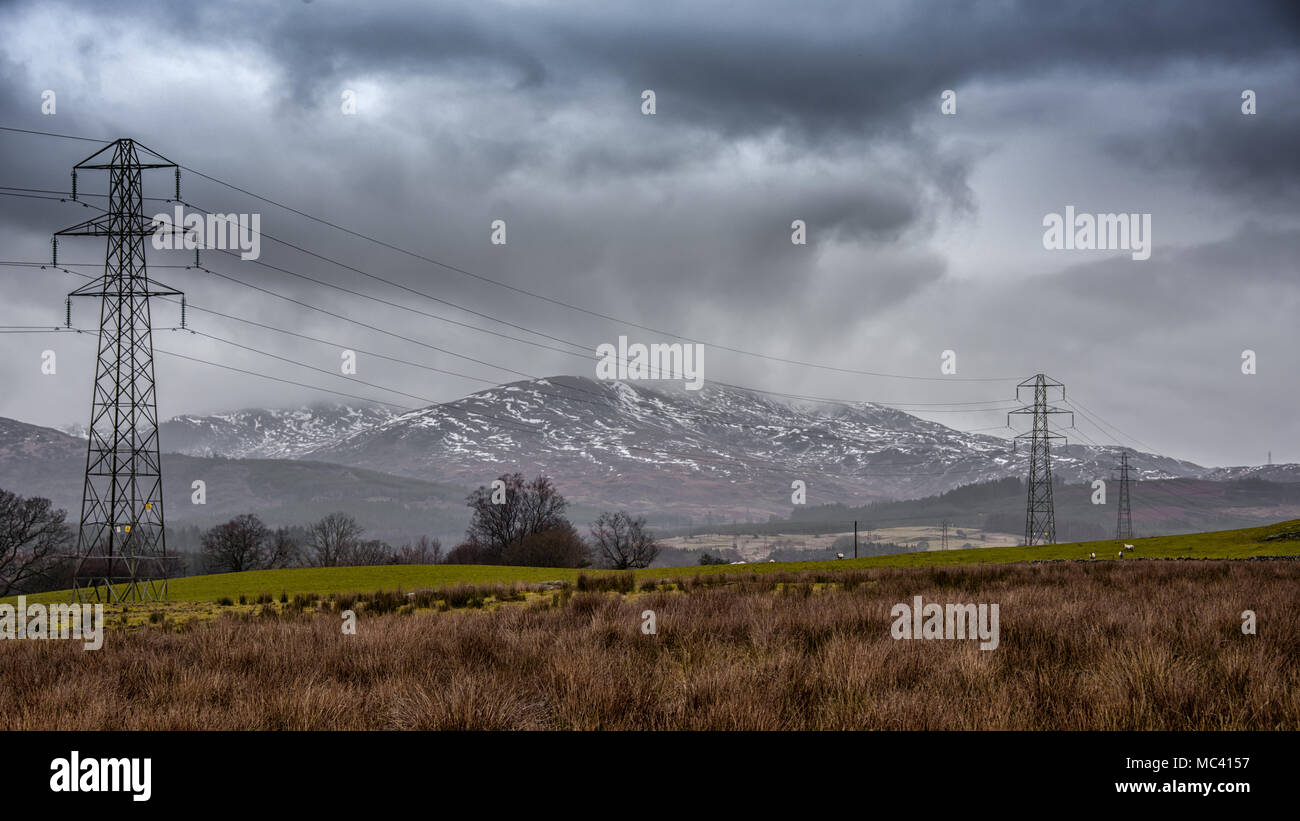 Un atormentado paisaje de Dumfries y Galloway en Escocia, con nieve en las montañas y torres eléctricas funcionan a través de la escena Foto de stock