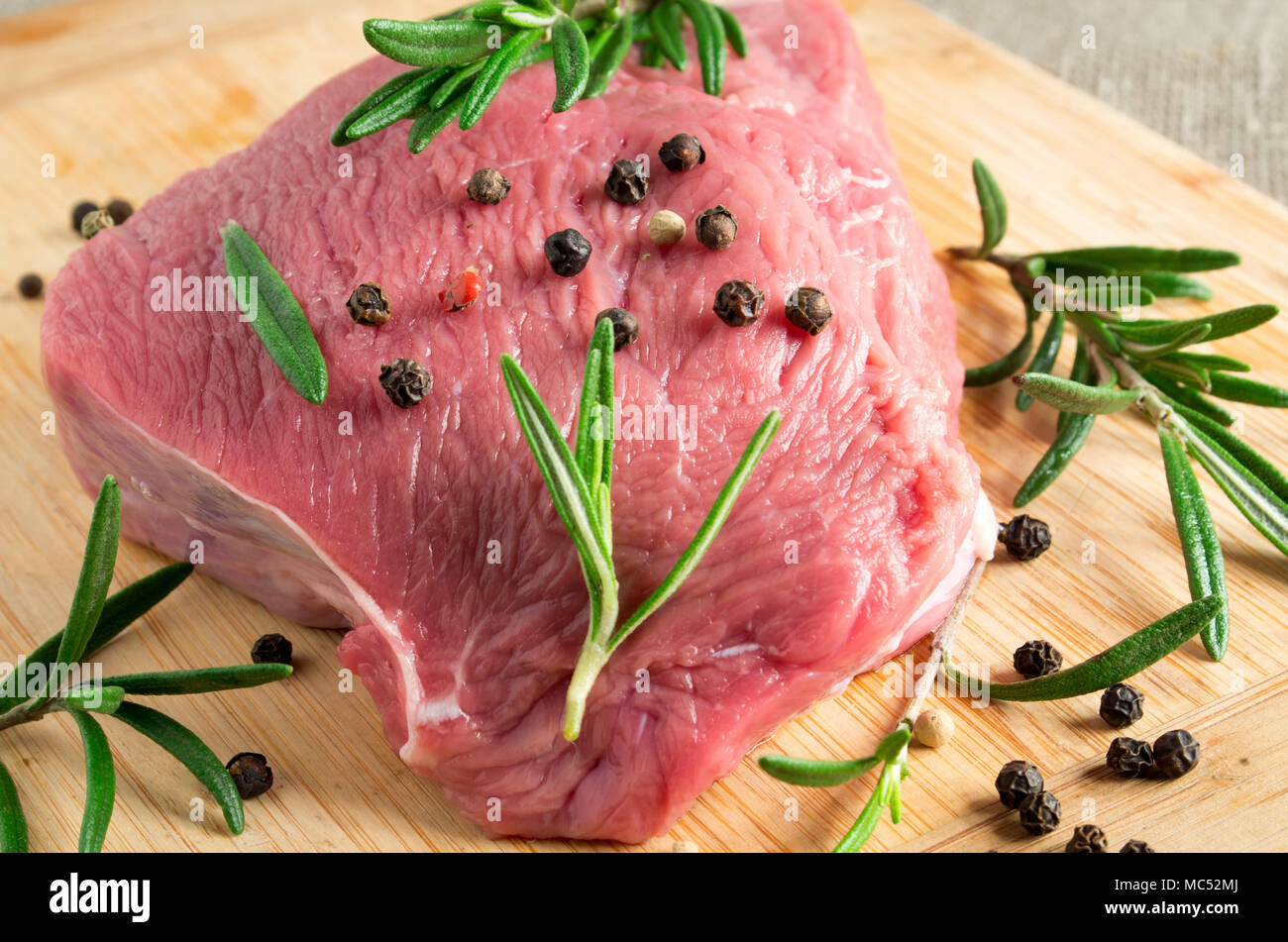 Trozo de carne cruda con romero y especias en la mesa de la cocina para cocinar los platos de carne Foto de stock