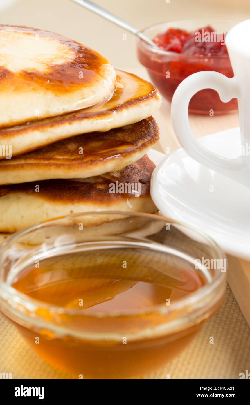 Tortitas con miel y mermelada y taza de té blanco para desayunar en una mesa de cerca Foto de stock