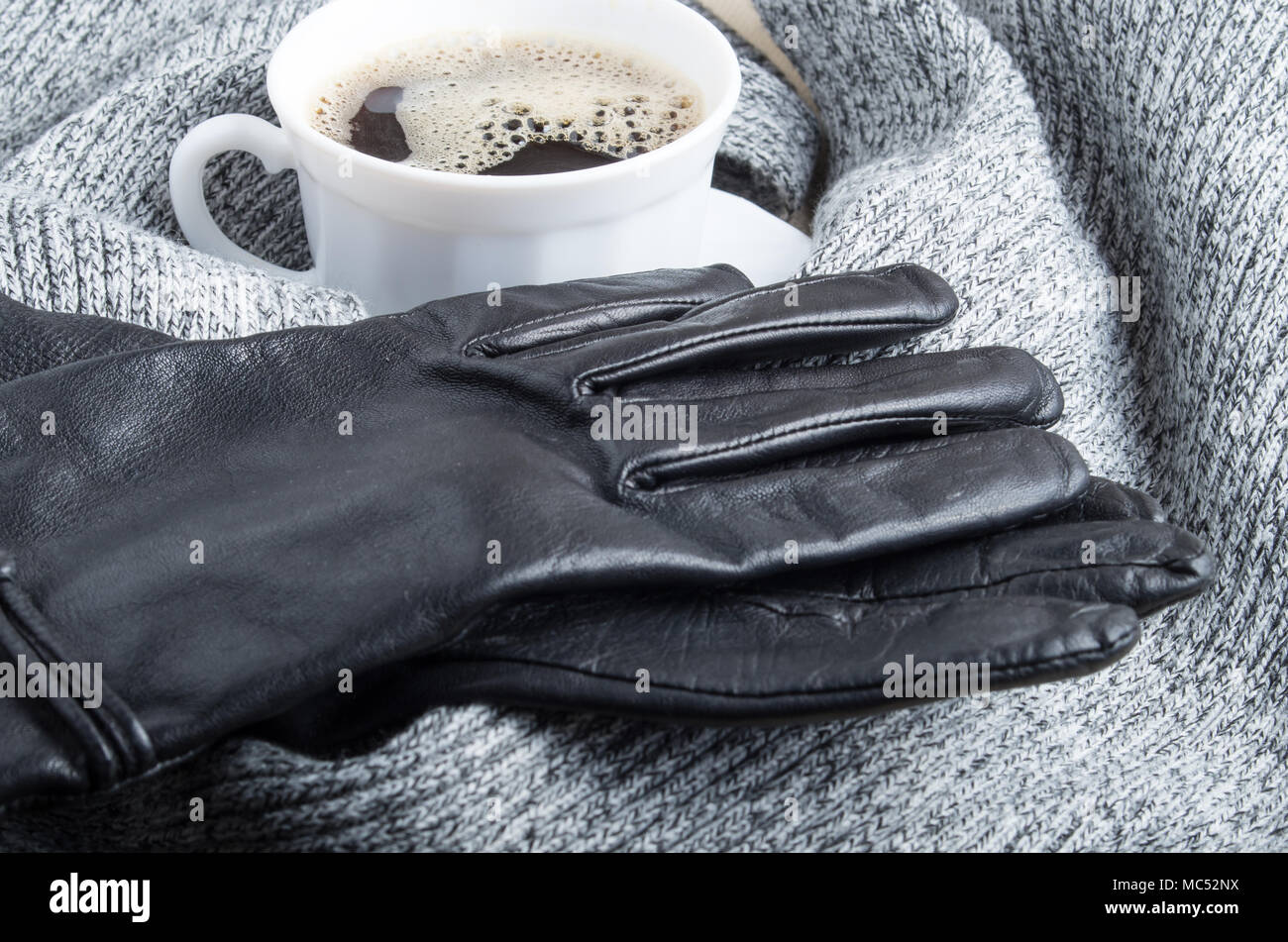 Gris bufanda de lana y guantes de cuero alrededor de la taza de café blanco con desenfoque y profundidad de enfoque Foto de stock