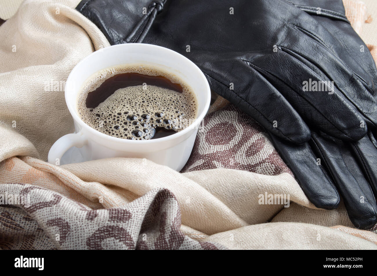 Blanco taza de café espresso en los pliegues de la mujer chales y guantes de cuero negro Foto de stock