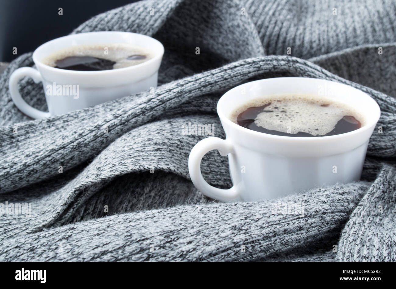 Dos tazas de café blanco envuelto en los pliegues de la bufanda de lana gris con una pequeña profundidad de enfoque. Foto de stock