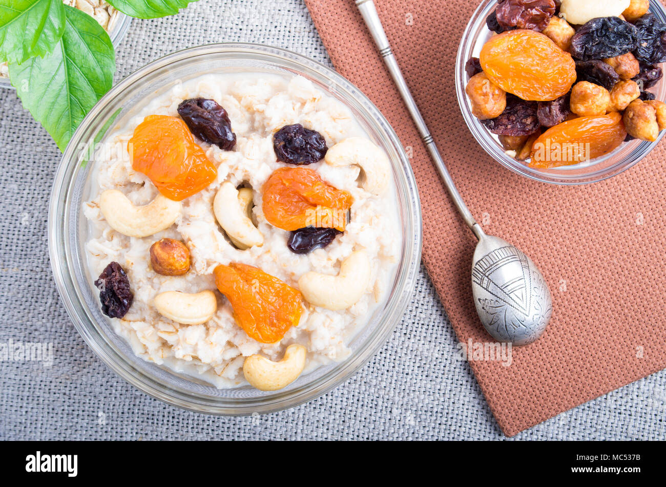 Vista superior de una porción de avena con frutas y bayas en un tazón de vidrio para desayunar en un mantel gris Foto de stock