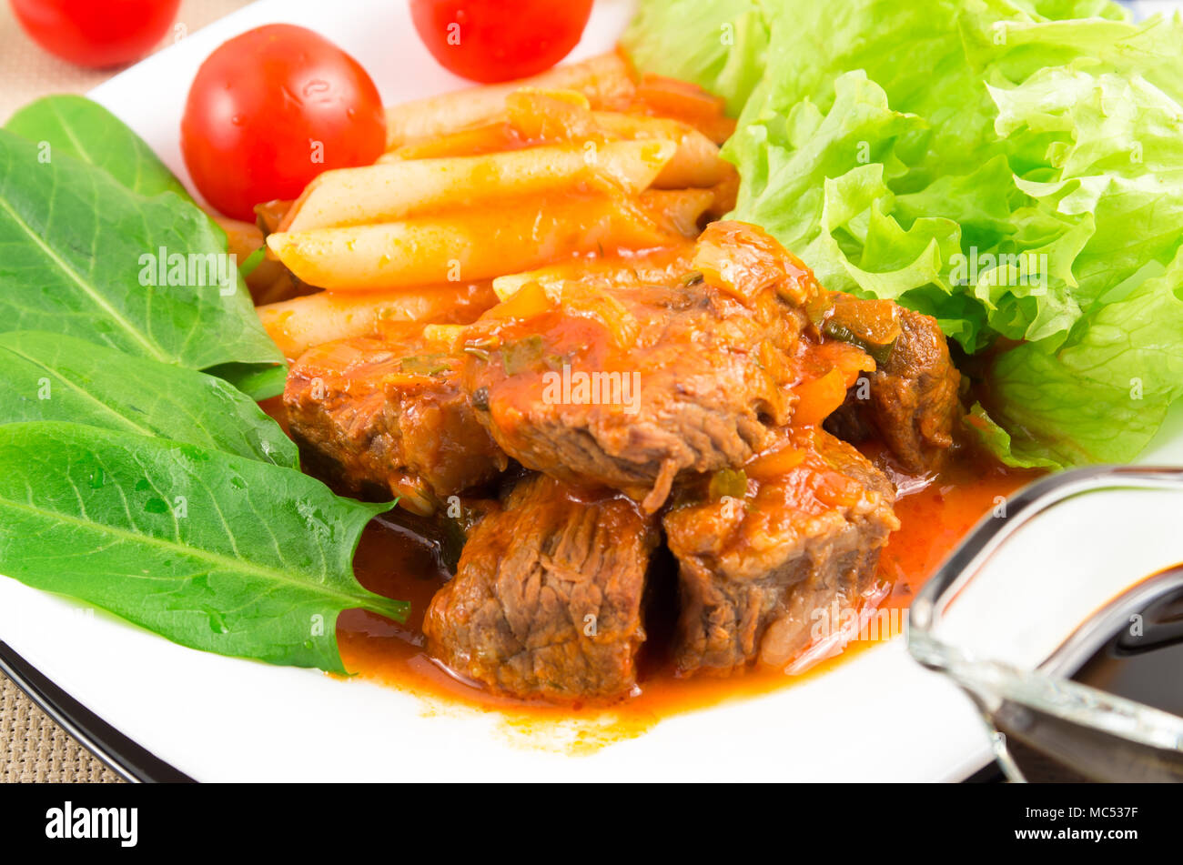 Ver de cerca en una comida de estofado de carne con pasta penne, lechuga y espinacas, servido en la mesa Foto de stock