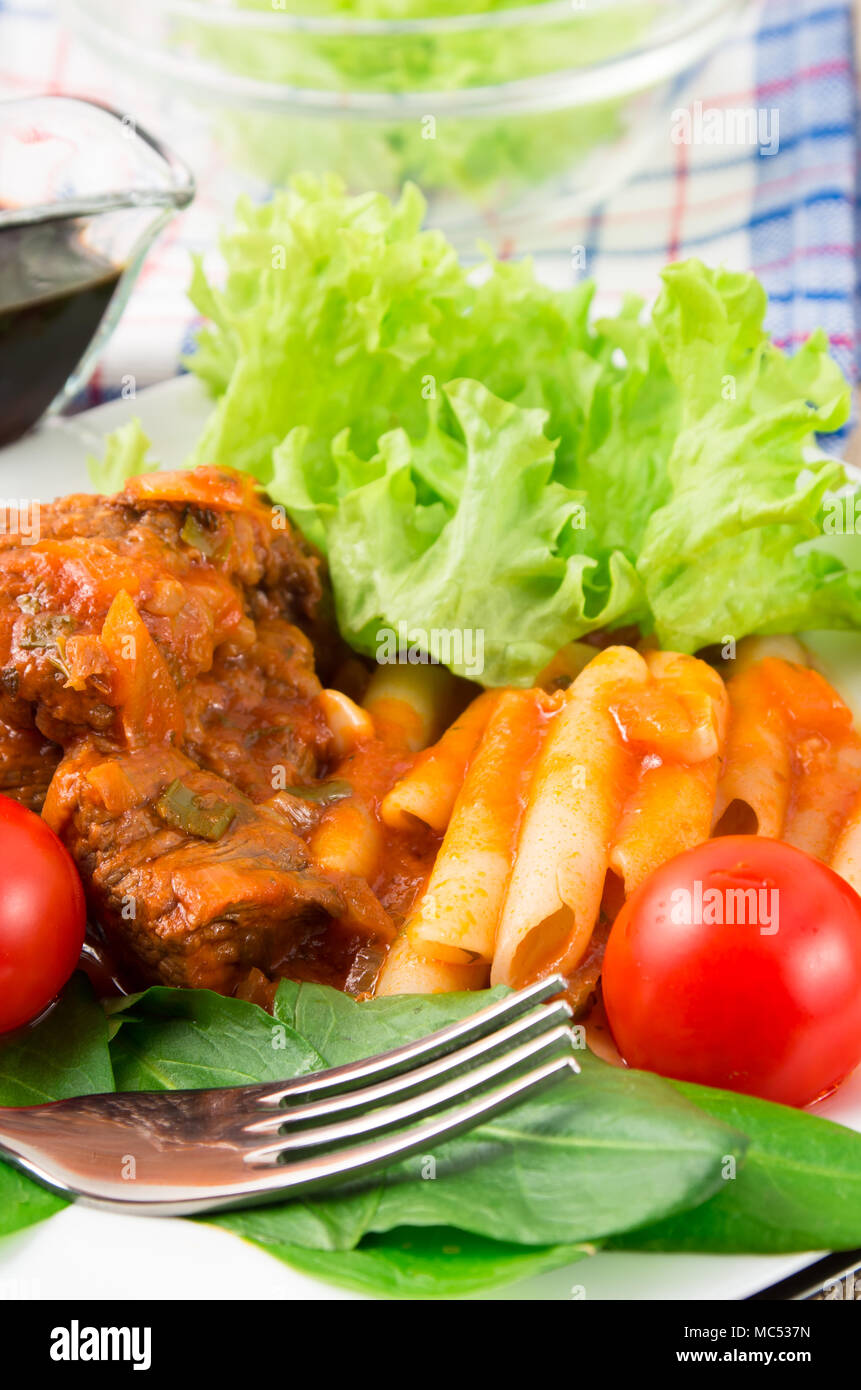 Ver de cerca en un plato de estofado de carne con pasta penne, tomates cherry y hierbas frescas con poca profundidad de enfoque. Foto de stock