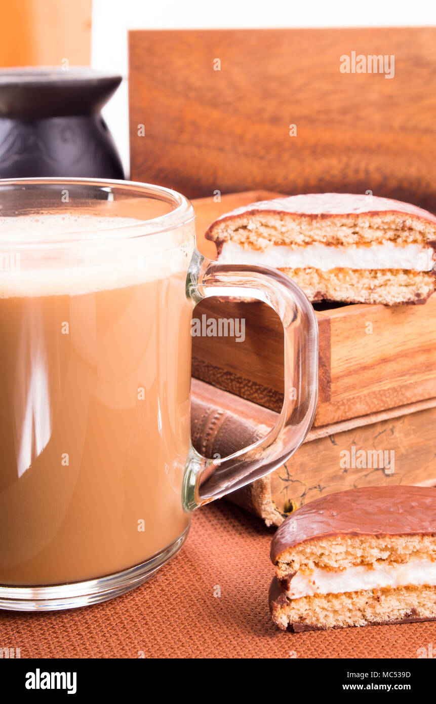 Jarra de cristal con chocolate caliente en una mesa cercana con viejos libros y galletas de chocolate en una bandeja de madera con poca profundidad de campo. Foto de stock