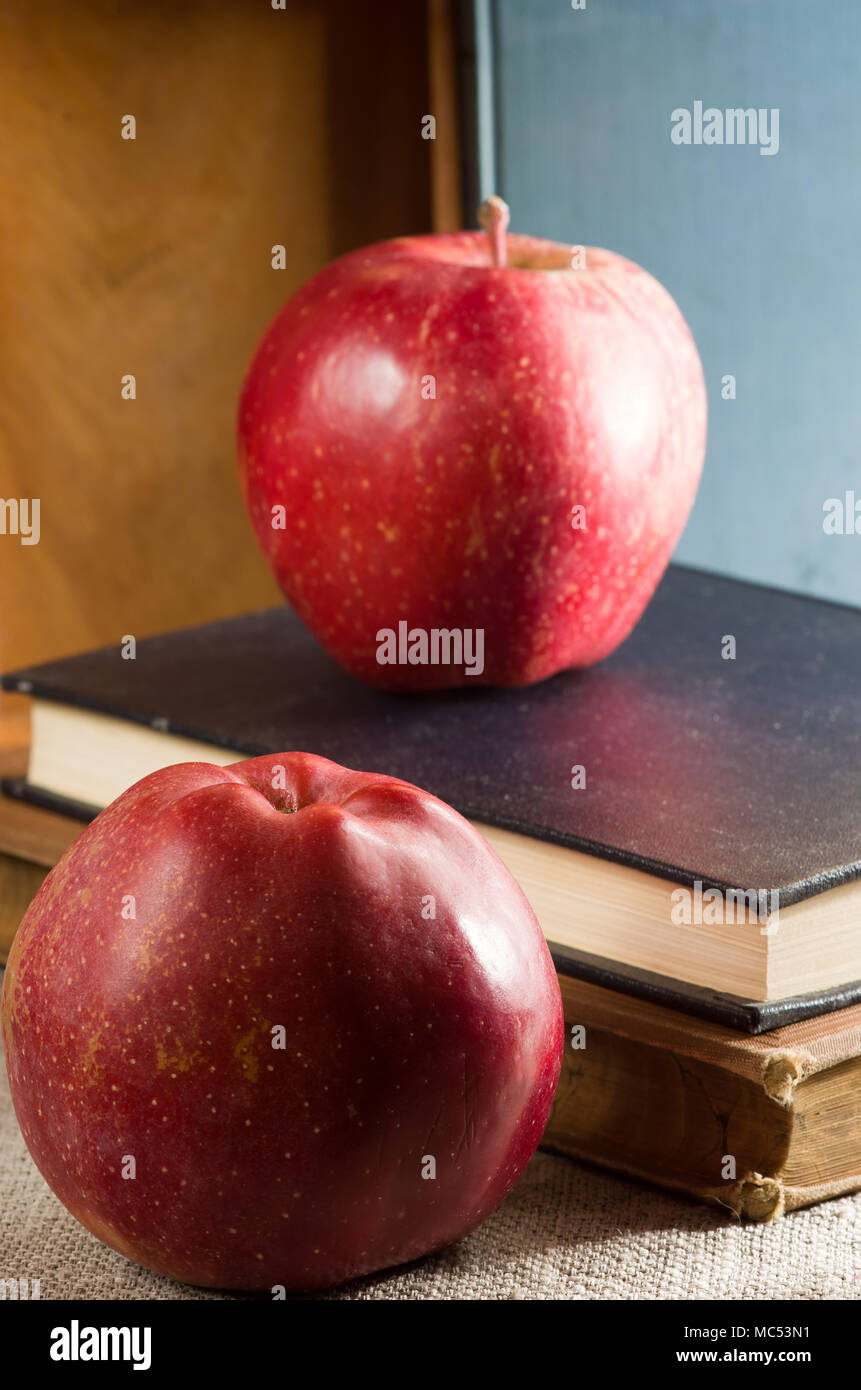 Dos manzanas rojas en un viejo vintage libros iluminados por una luz brillante desde la ventana con poca profundidad de campo. Foto de stock