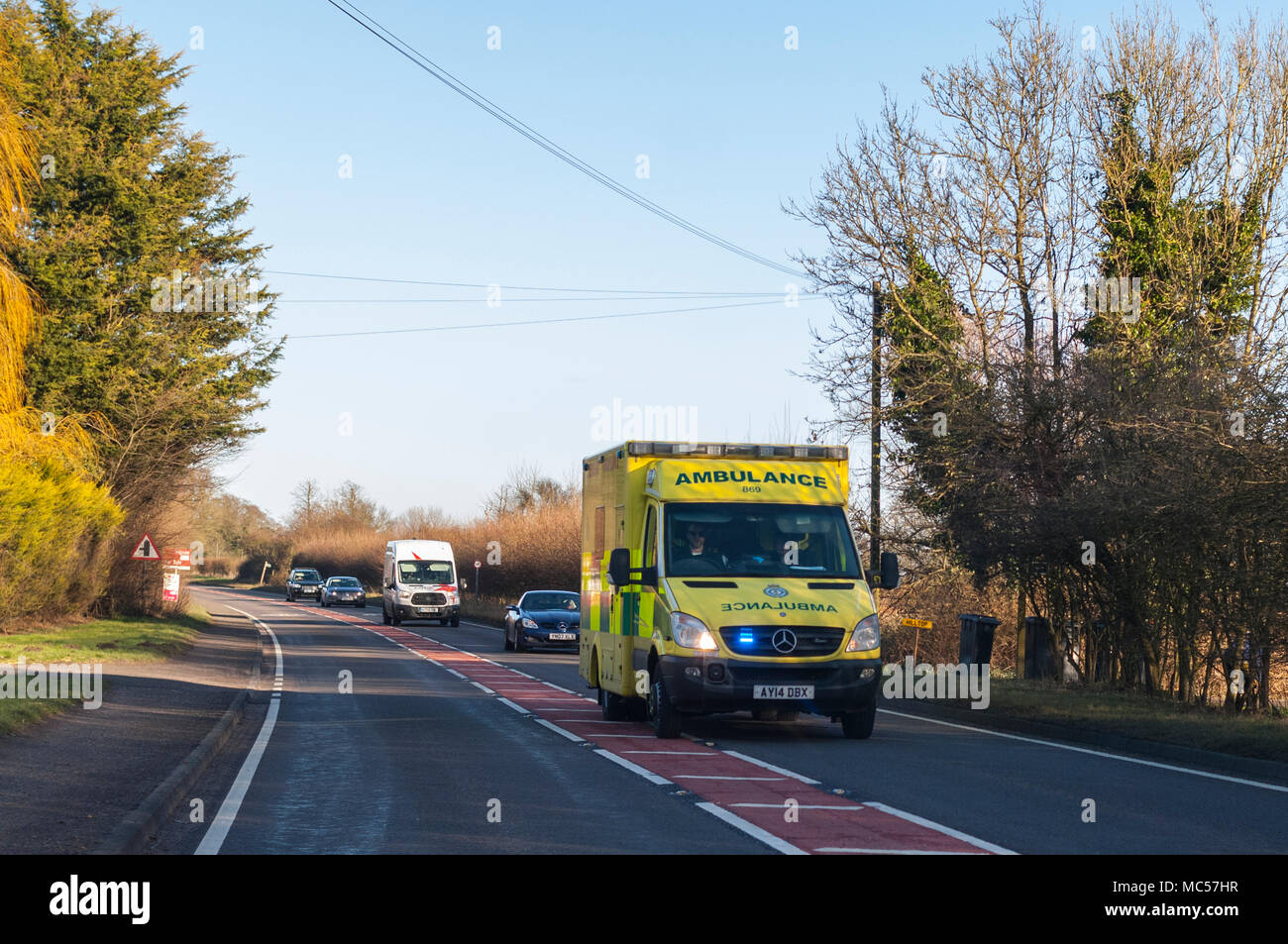 Una ambulancia con las luces azules destellando en una carretera principal, en Suffolk, Inglaterra, Reino Unido Foto de stock