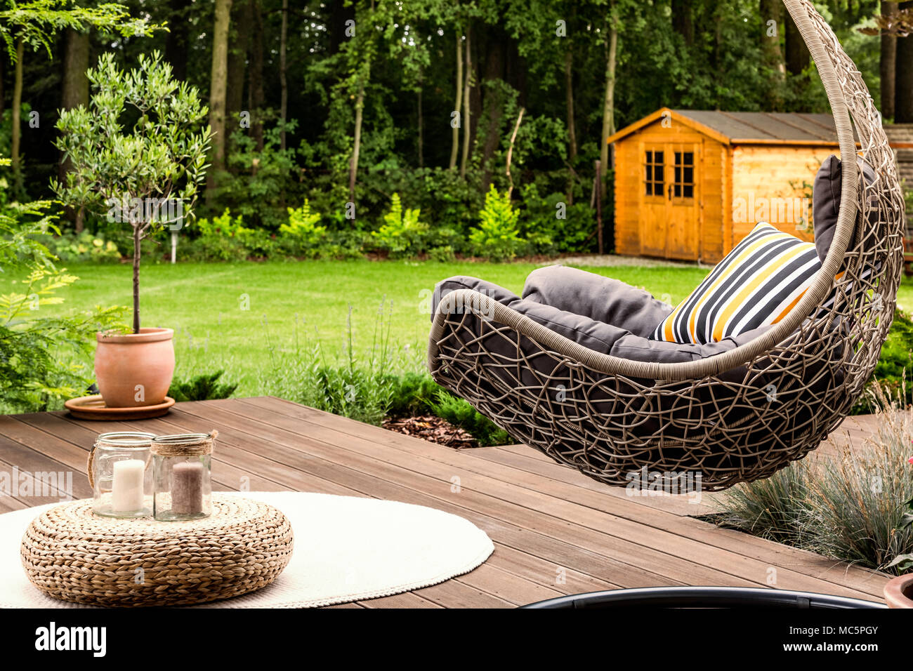 Pouf sobre alfombra redonda blanca junto a una silla colgante en el jardín de una casa Foto de stock