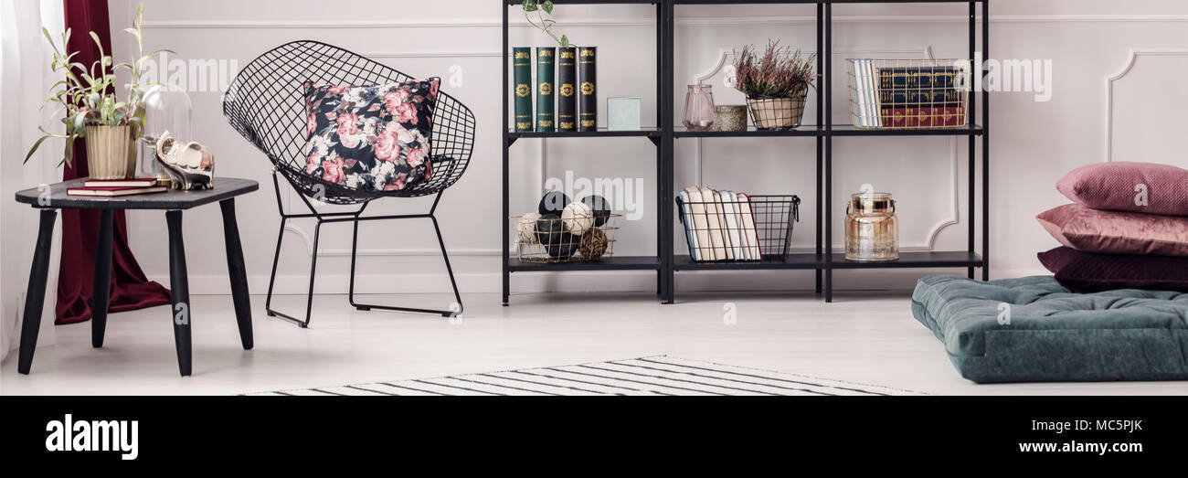 Panorama de un lujoso apartamento interior con silla de alambre negro, almohadas, librería y elegante decoración Foto de stock