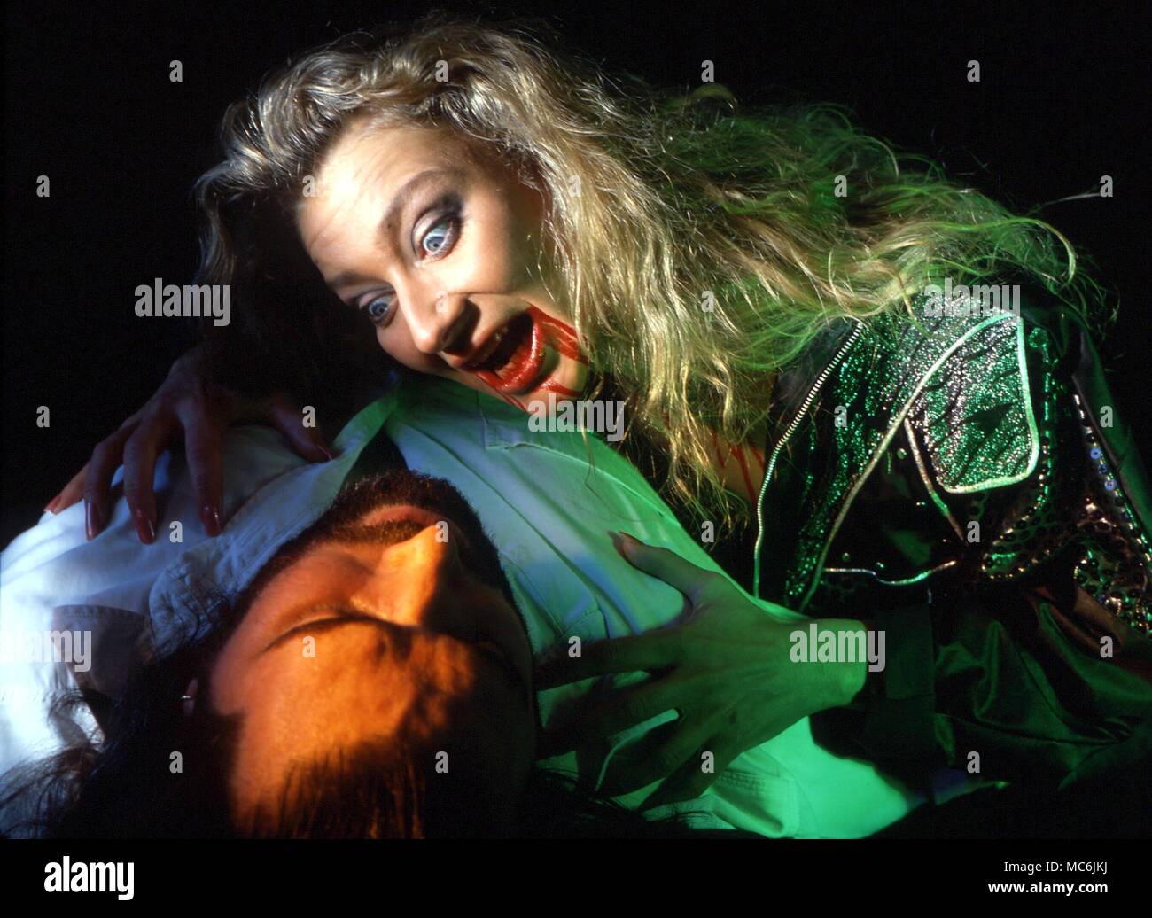 DRACULA - Hembra Drácula, o vampiro con sangre en su boca, atacando a una víctima masculina Foto de stock