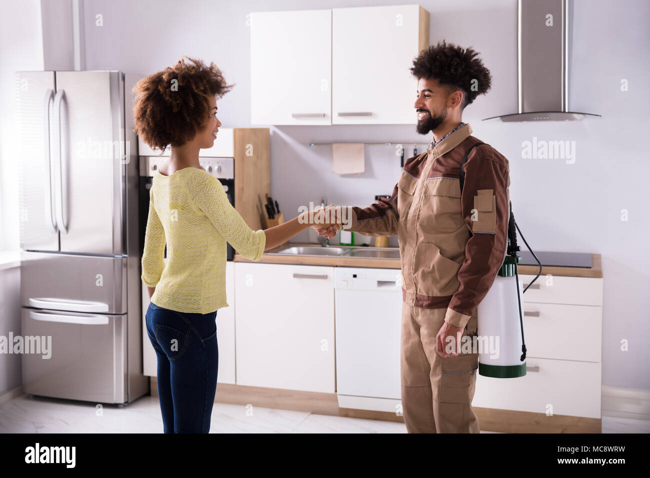 Control de Plagas macho trabajador un apretón de manos con una mujer feliz en la cocina doméstica Foto de stock