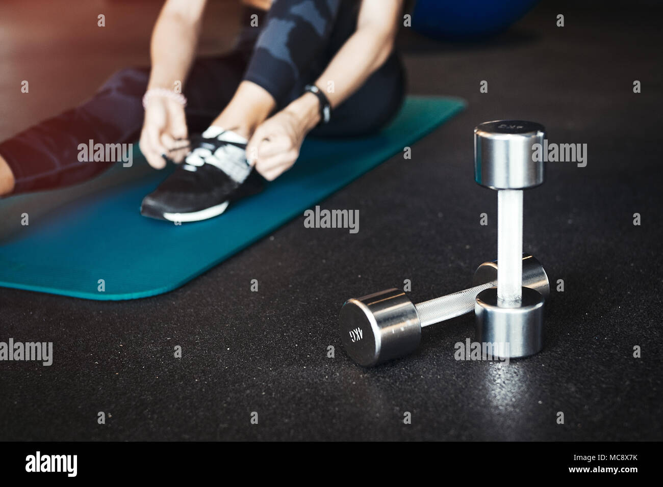 Joven morena atractiva chica enlacing su calzado deportivo después de practicar ejercicio y entrenamiento crossfit sobre azul esterilla de yoga. La mujer está en backgroun borrosa Foto de stock