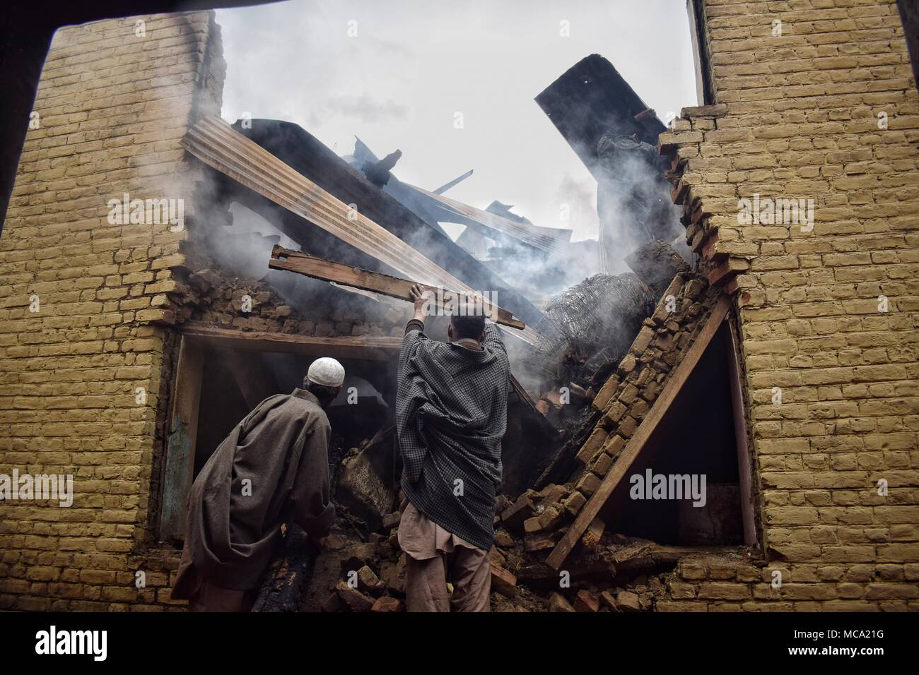 Los lugareños borrado quemando cosas de casas que fueron destruidas por las fuerzas indias en una zona Khudwani Gunbattle al sur del distrito de Cachemira Kulgam el 11 de abril de 2018. Cuatro civiles y 1 hombre del ejército fueron muertos y cerca de 150 civiles fueron heridos en enfrentamientos durante el encuentro Foto de stock