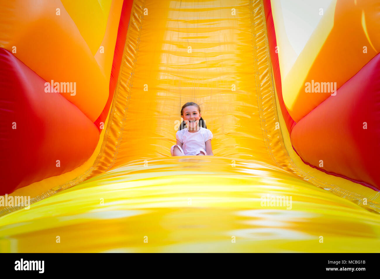 Niña feliz tener mucha diversión en el salto de un castillo mientras se desliza. Foto de stock