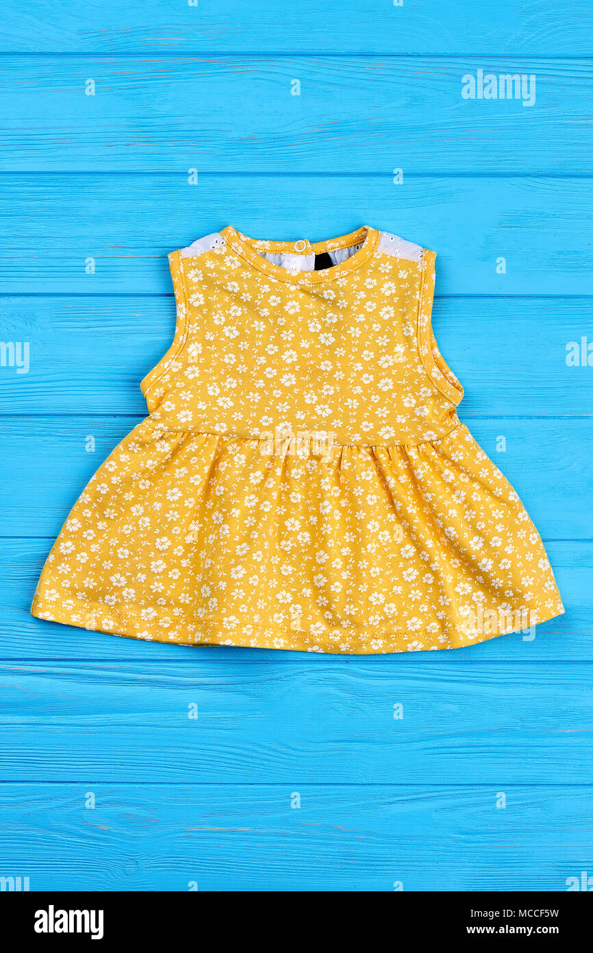 Bellos y coloridos sundress para bebé niña. Poco vestido amarillo con  patrón de pequeñas flores blancas para el recién nacido, azul de fondo de  madera Fotografía de stock - Alamy