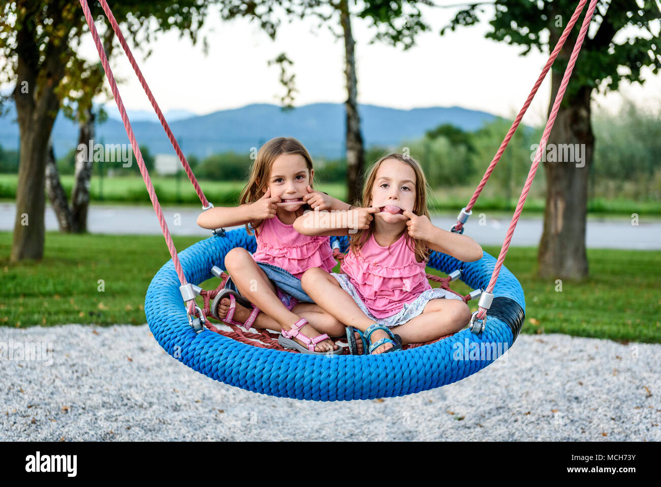 Dos gemelas en tela de araña nido swing en playground. Los niños activos jugando con columpio gigante-N-Slide Swing Web Monster en juegos al aire libre Foto de stock