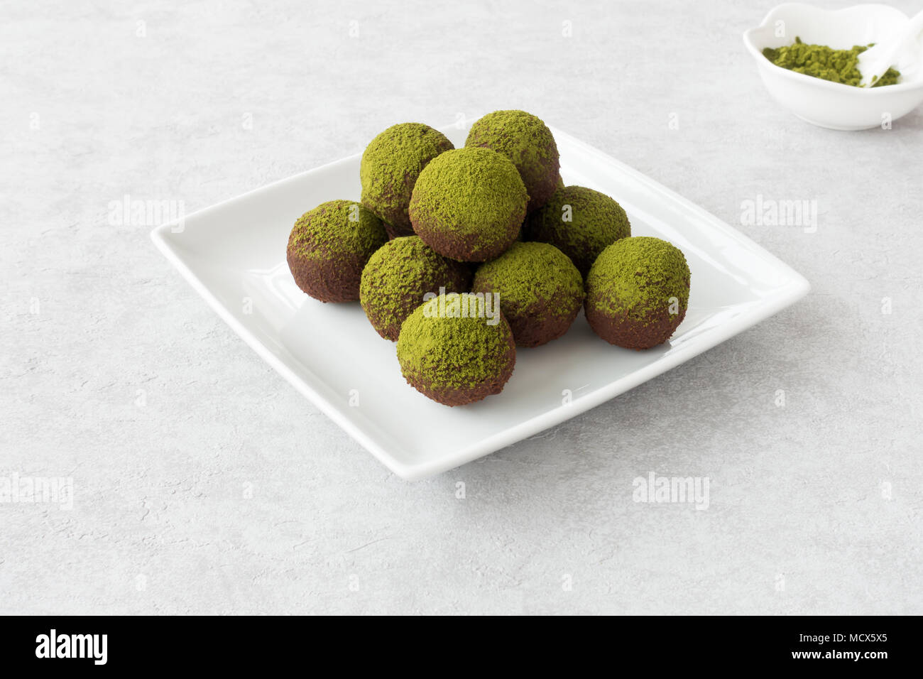 Trufas de chocolate caseras espolvoreado con polvo matcha verde dispuesto sobre una placa blanca. Foto de stock