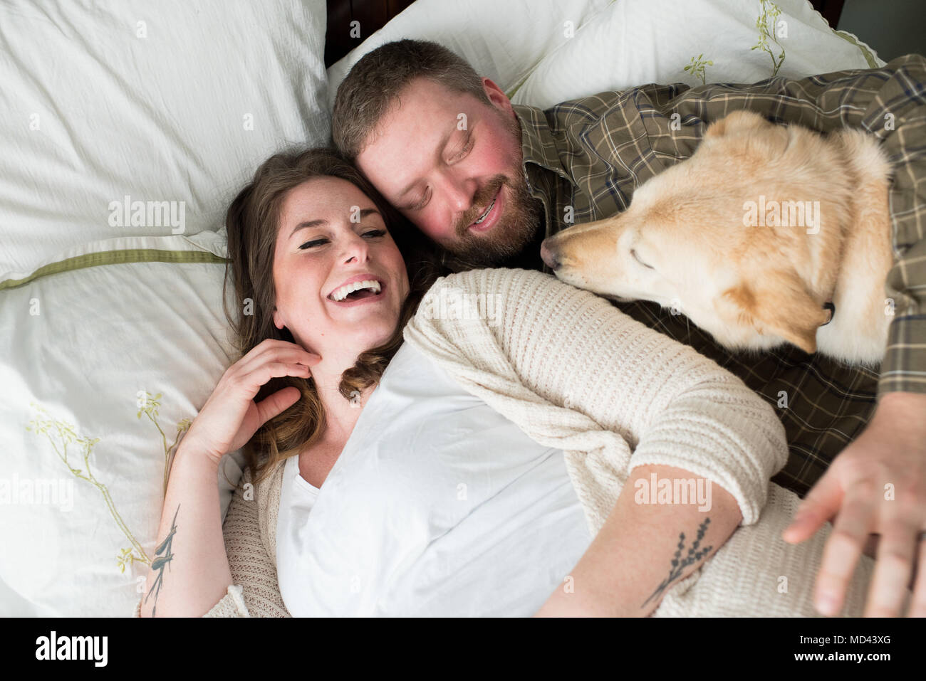 Mujer embarazada acostado en la cama con la pareja, perro tumbado en la cama junto a ellos, vista elevada Foto de stock