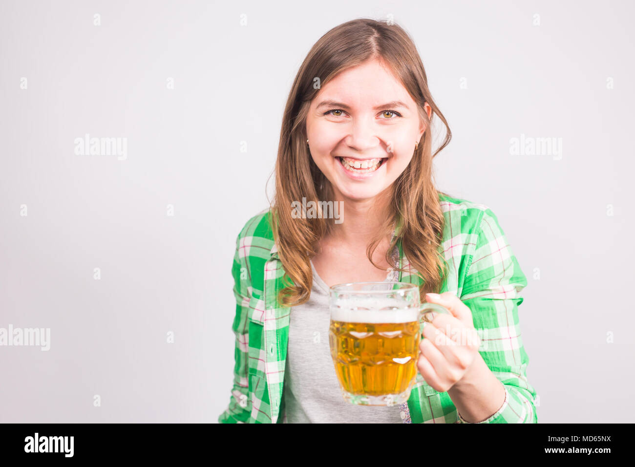 Joven alegre sosteniendo una jarra de cerveza llena de cerveza y sonriendo sobre fondo blanco. Foto de stock