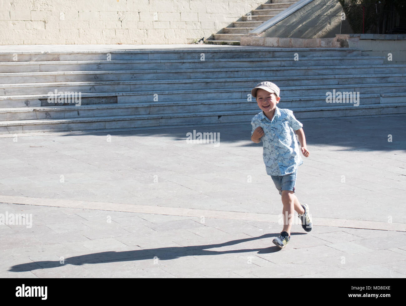Poco feliz niño corriendo en la calle enfrente de la escalera, Heraklion, Grecia Foto de stock