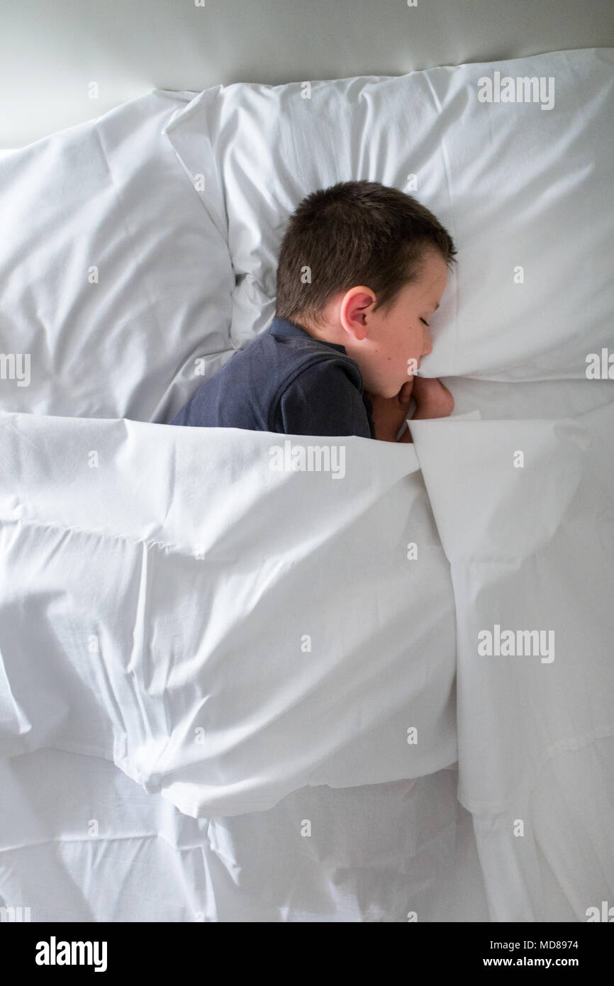 Niño durmiendo en cama con manta Foto de stock