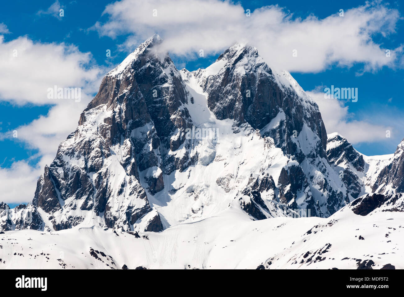 La parte superior de la montaña Ushba, alrededor de 4700 m, contra el cielo azul con nubes preciosos. Primer plano de la famosa doble pico del Cáucaso. Svaneti, Georgia. Foto de stock